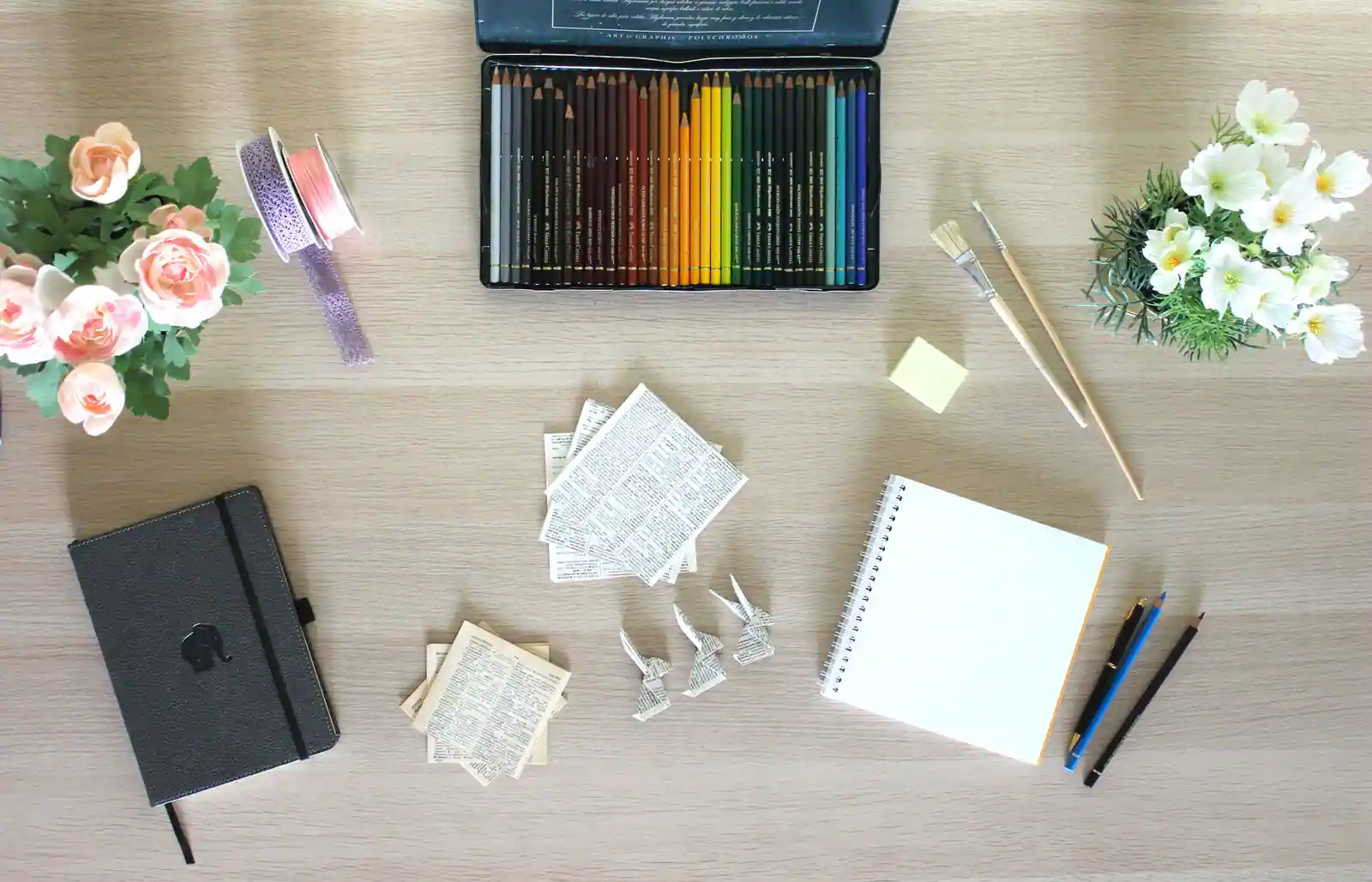 Crayons de couleur, pinceau, carnet et papier plié sur une table, matériel de loisirs créatifs.